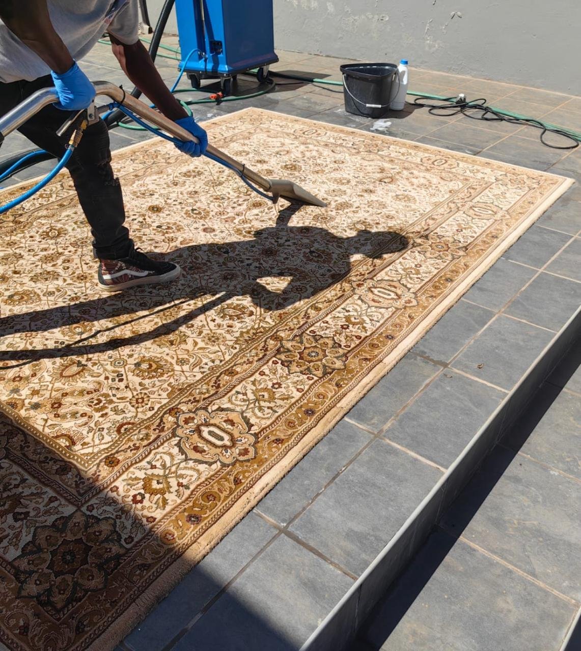 Worker using extraction equipment to clean a patterned rug outdoors