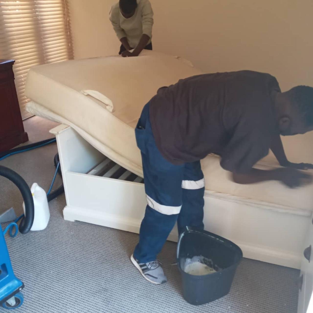 Cleaner lifting a mattress while working inside a bedroom