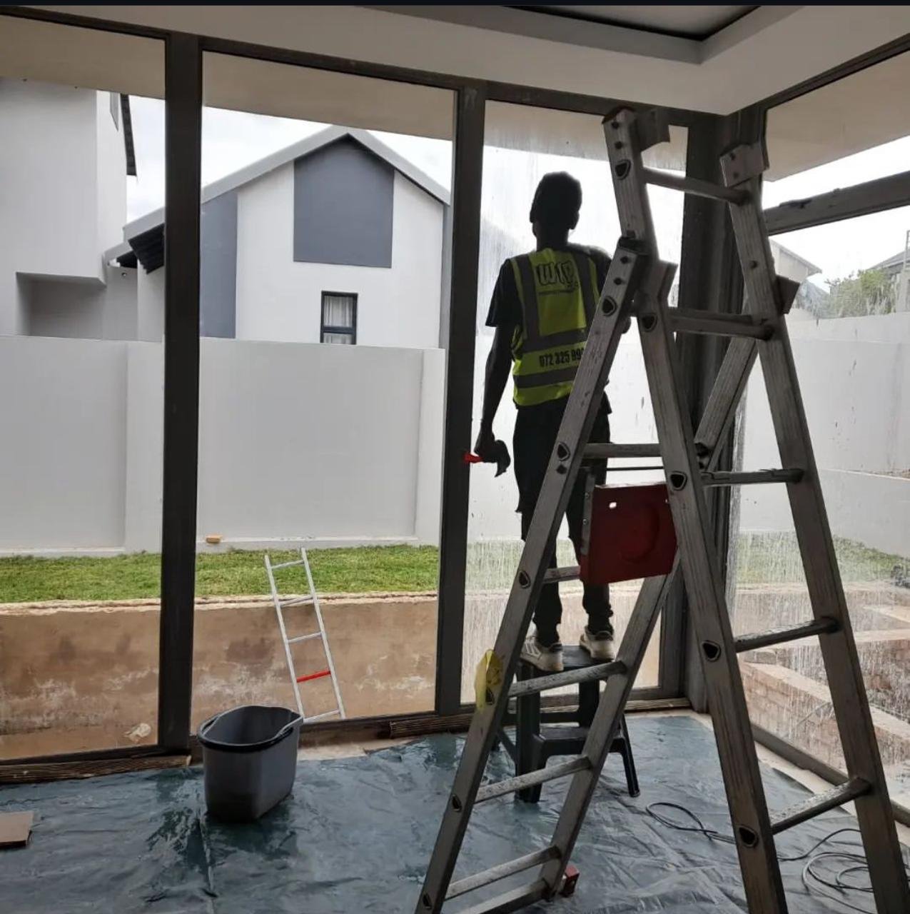 Cleaner washing a large interior glass window with ladders in place