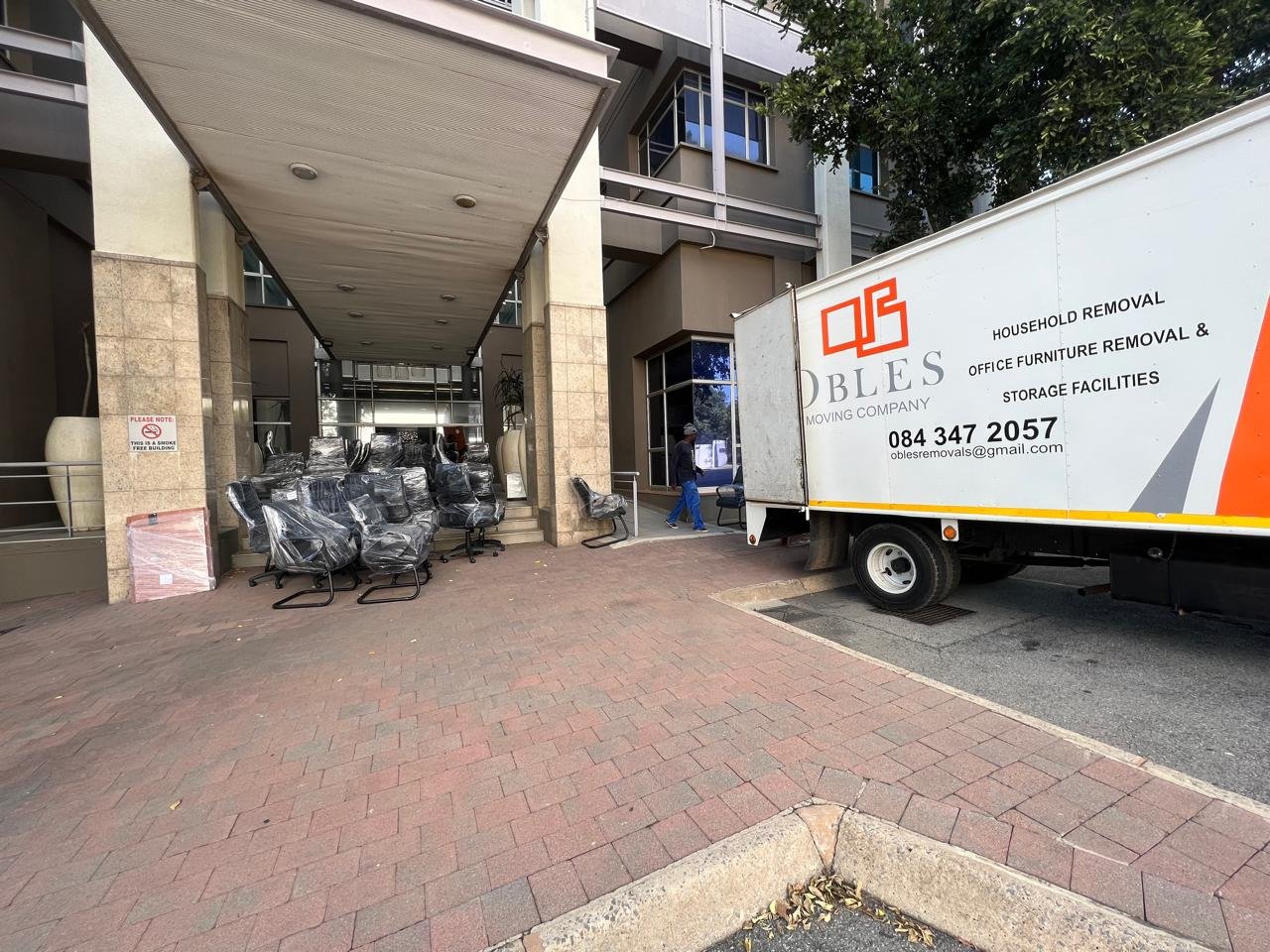 Wrapped office chairs lined up outside a building next to an Obles Removals truck