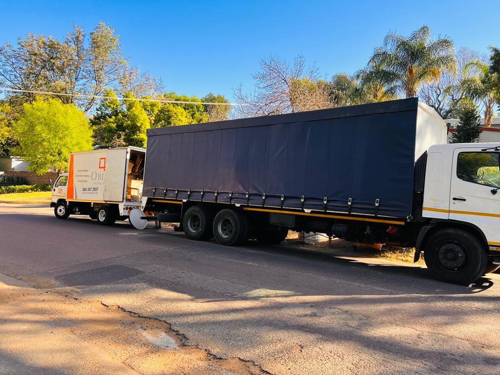 Large covered truck parked behind an Obles Removals truck on a tree-lined street