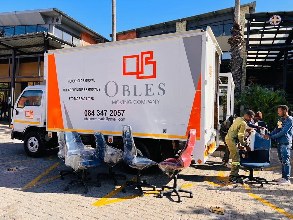 Obles Removals truck parked while office chairs are being loaded outside a building